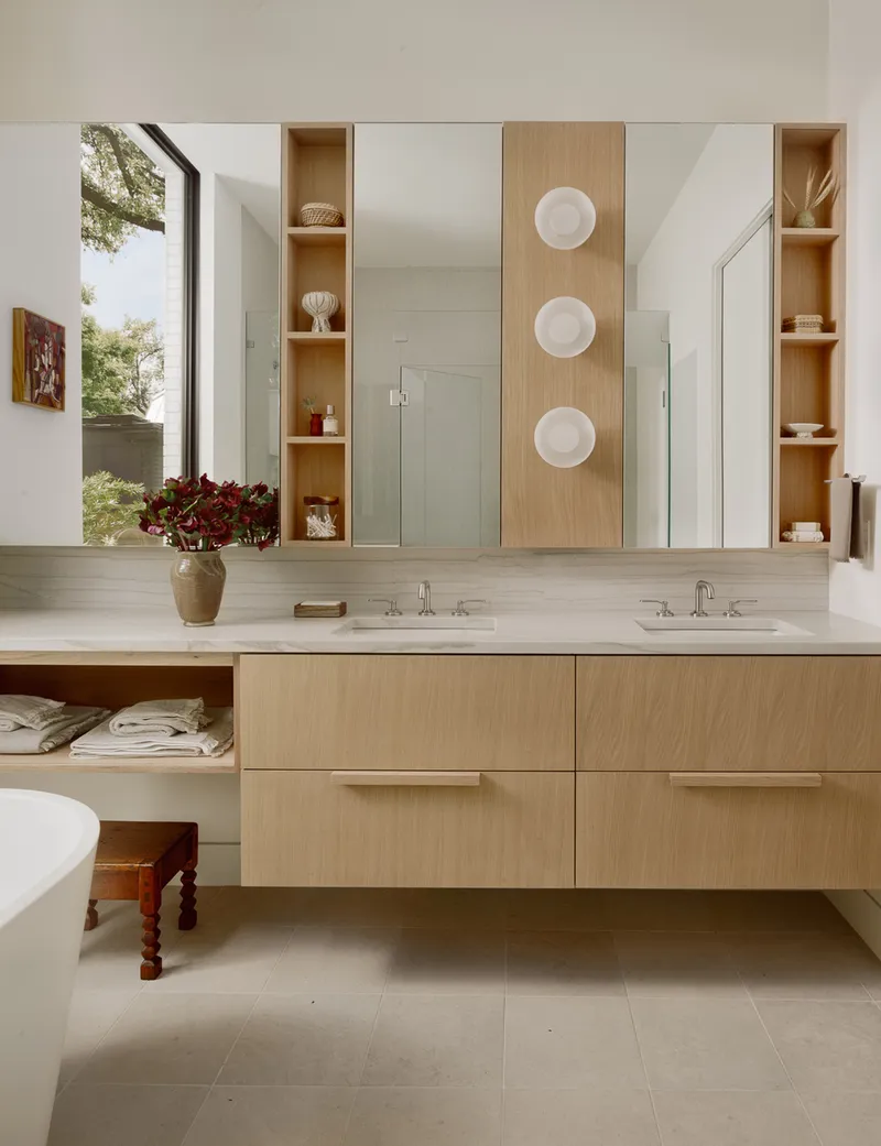 Bathroom vanity with light wood cabinetry and white stone countertop flanked by open shelving units