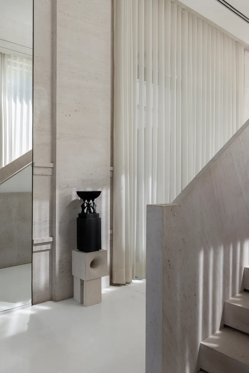 Interior view showing stone walls, vertical curtains, and a black sculpture on a pale plinth
