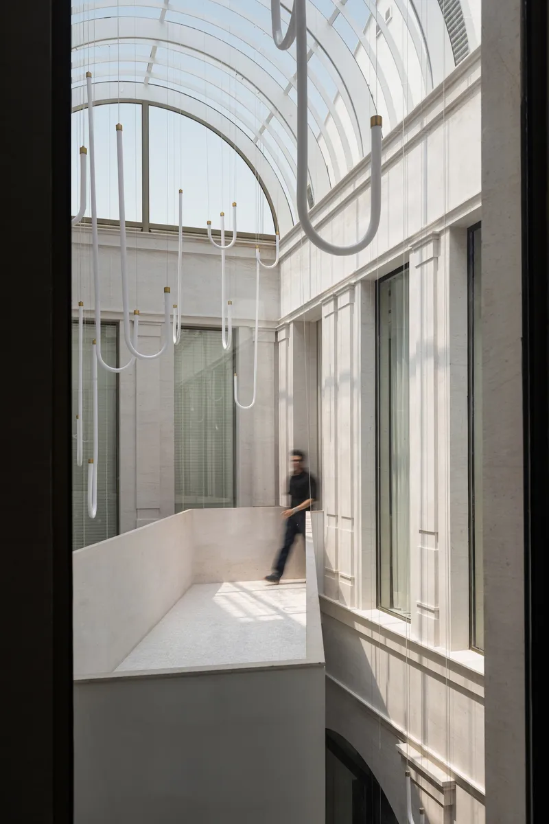 Interior courtyard with curved glass roof, linear pendant lights, and a figure crossing the bridge