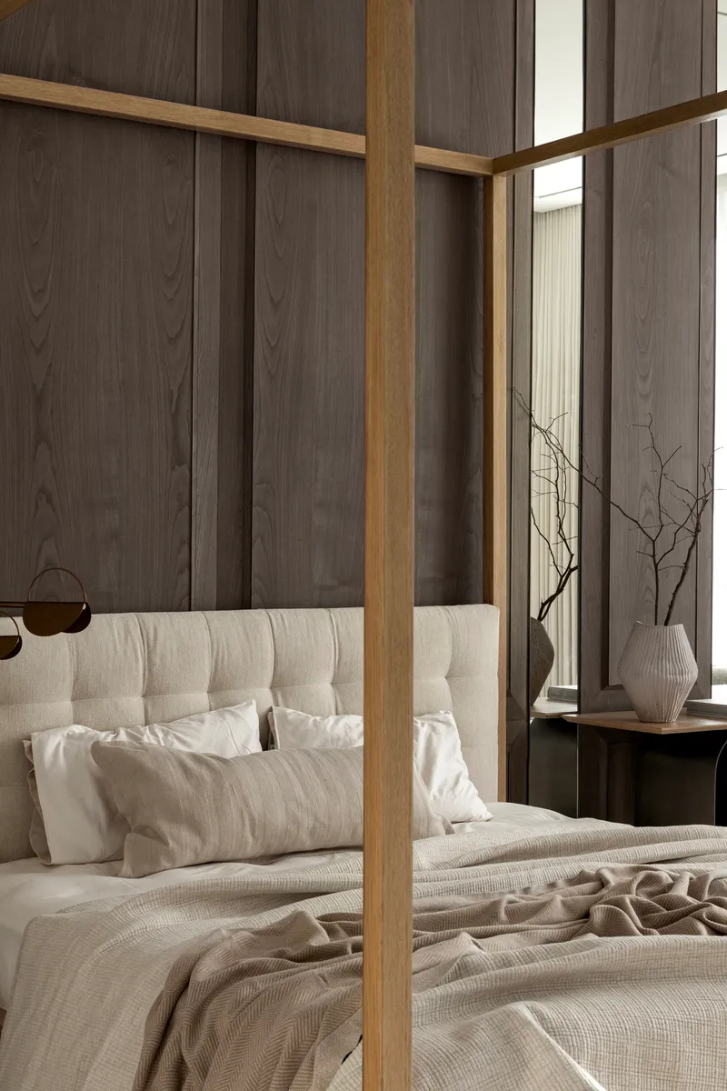 Bedroom with timber-framed canopy bed against dark wood paneled walls and sheer curtains