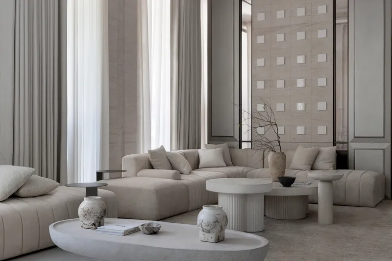 Double-height living room with floor-to-ceiling curtains and grey upholstered seating around circular tables
