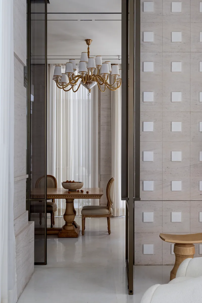 View through bronze-framed glass doors to dining room with brass chandelier and stone grid wall