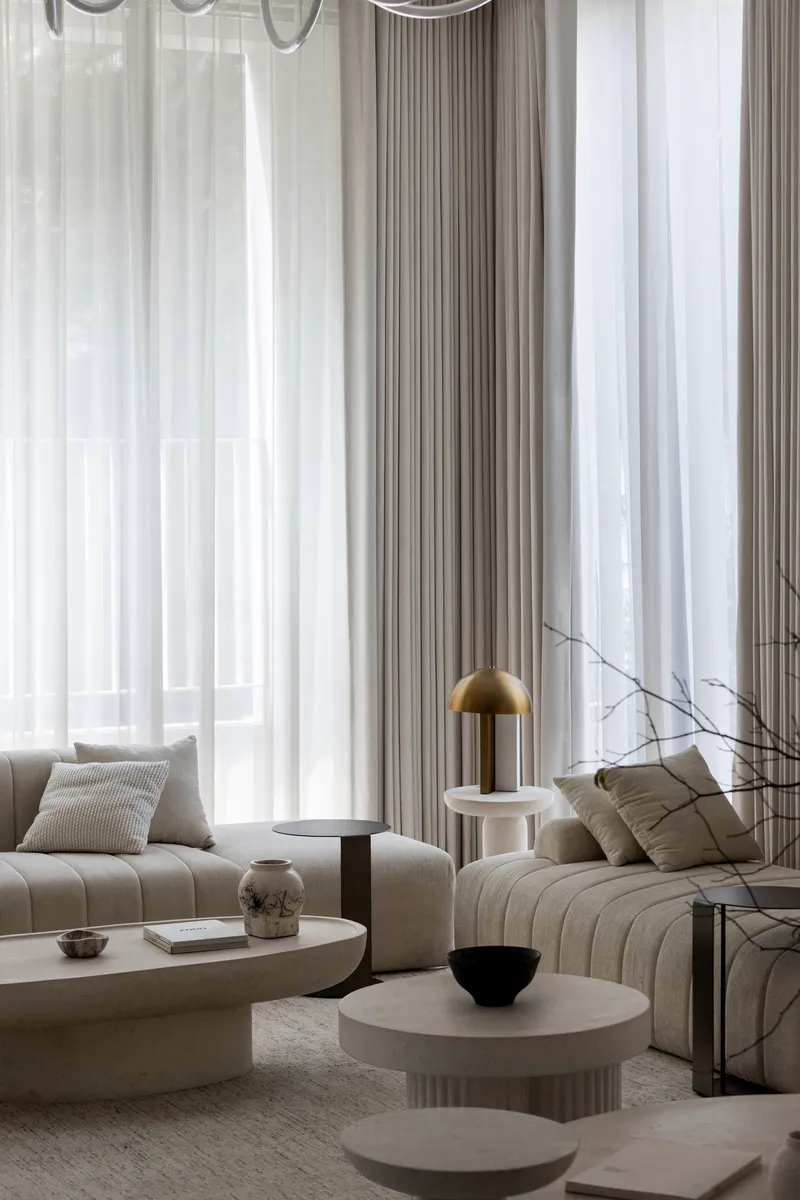 Living area with layered sheer curtains filtering daylight over modular seating and fluted stone tables