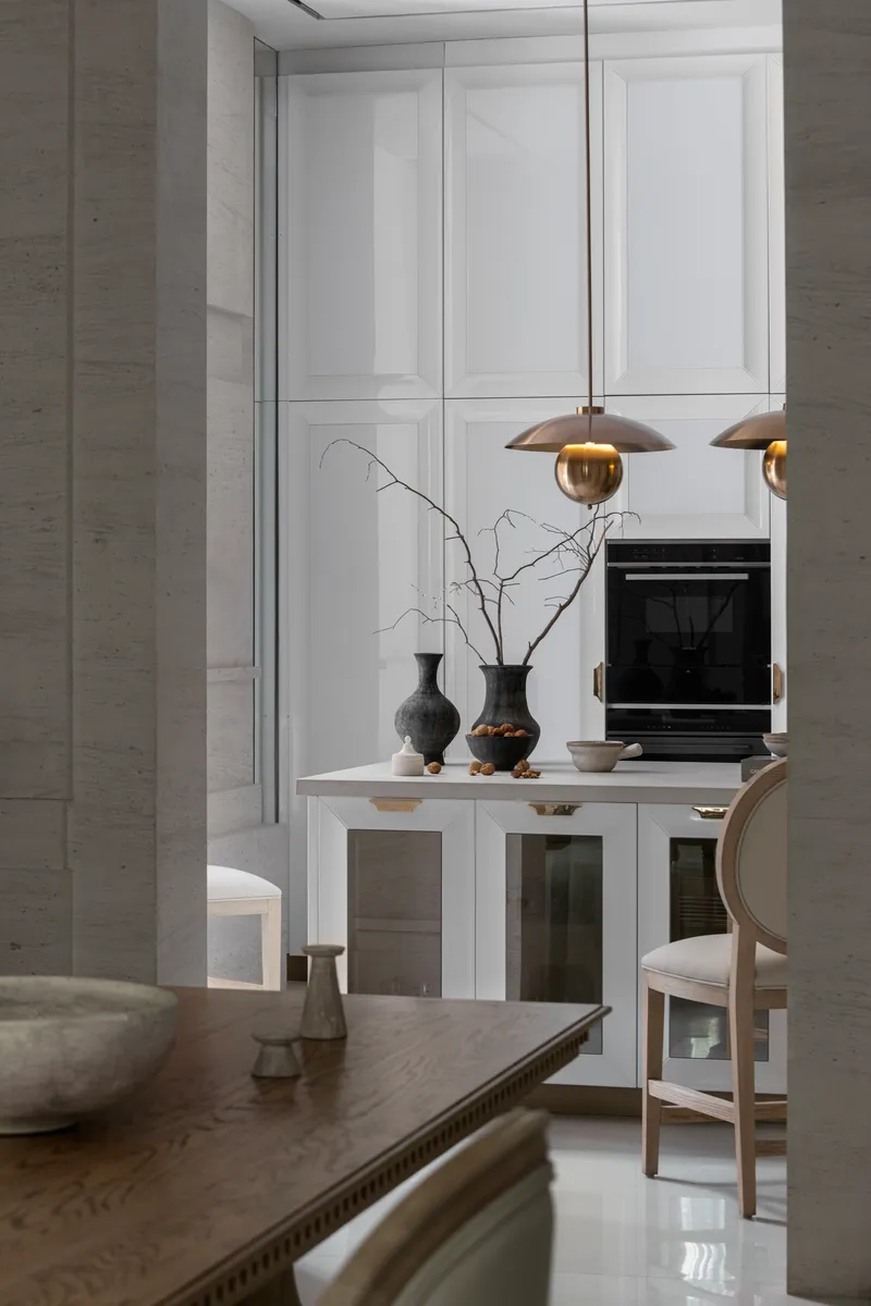 Kitchen island with brass pendant lights and decorative branches against white paneled cabinetry