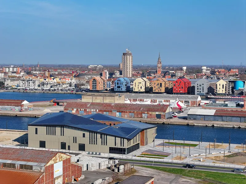 Aerial view of the low-slung building with dark pitched roof along the waterfront beneath clear blue sky
