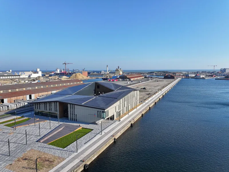 Elevated view showing the angular solar panel roof and vertical window patterns beside the harbor