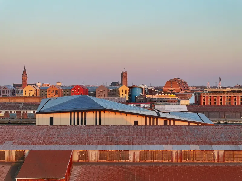 Roofscape perspective with the solar panel roof volume emerging above brick warehouse rooftops at twilight