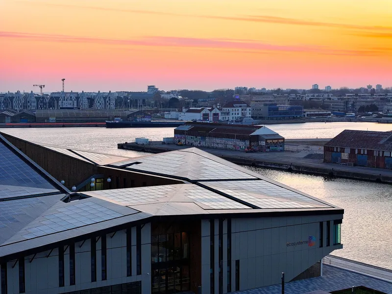 Rooftop view of the angled photovoltaic panels and glazed facade overlooking the waterfront at sunset