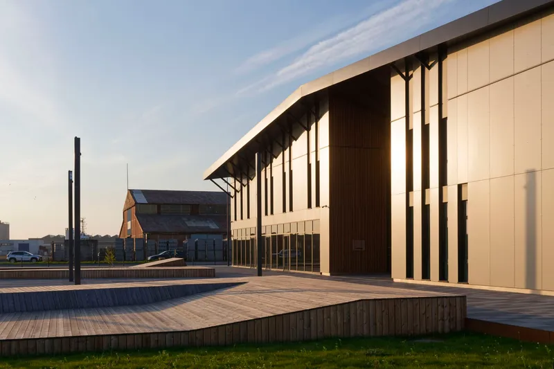 Timber-decked plaza in front of the slatted facade with deep overhang at golden hour
