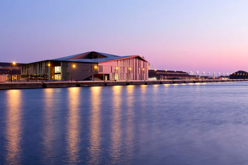Long waterfront elevation with illuminated windows and slat detailing under a violet twilight sky