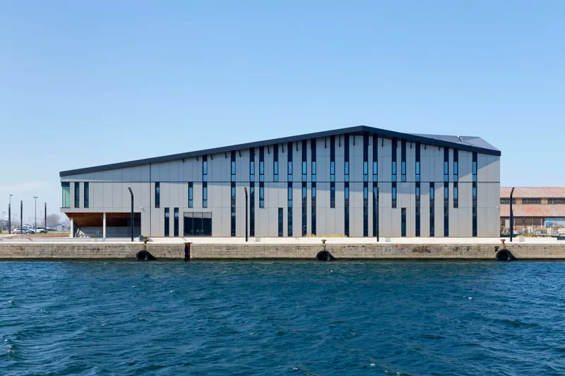 Waterside elevation with vertical window slots and metal cladding seen from across the harbor