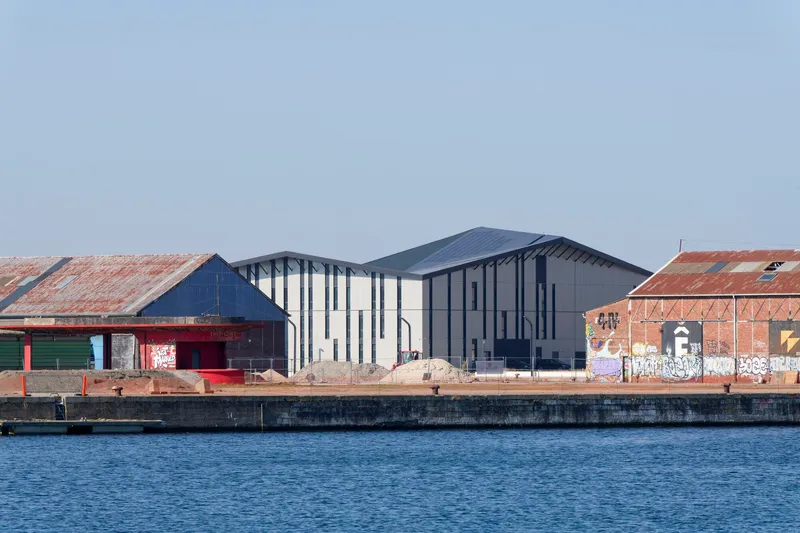 Cluster of pitched-roof volumes with varied cladding beside weathered brick warehouses along the quay