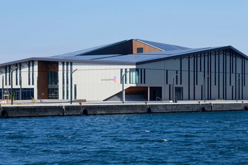 Waterfront facade with vertical metal fins and clerestory timber volume under a clear sky