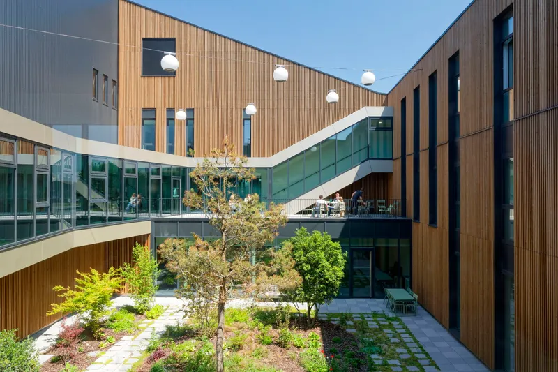 Interior courtyard with planted beds and timber-clad volumes framing a glazed upper walkway