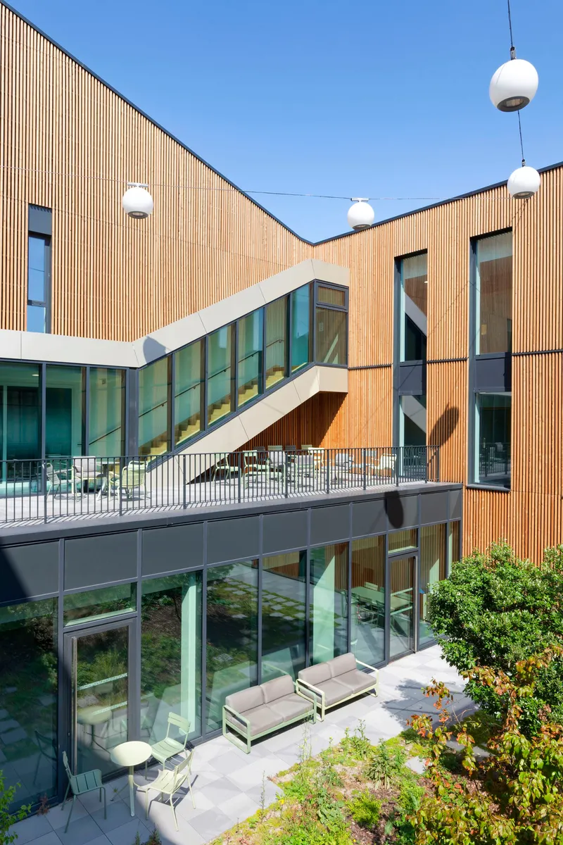 Timber-clad facades flanking a diagonal glazed stair volume with suspended globe lights above the courtyard