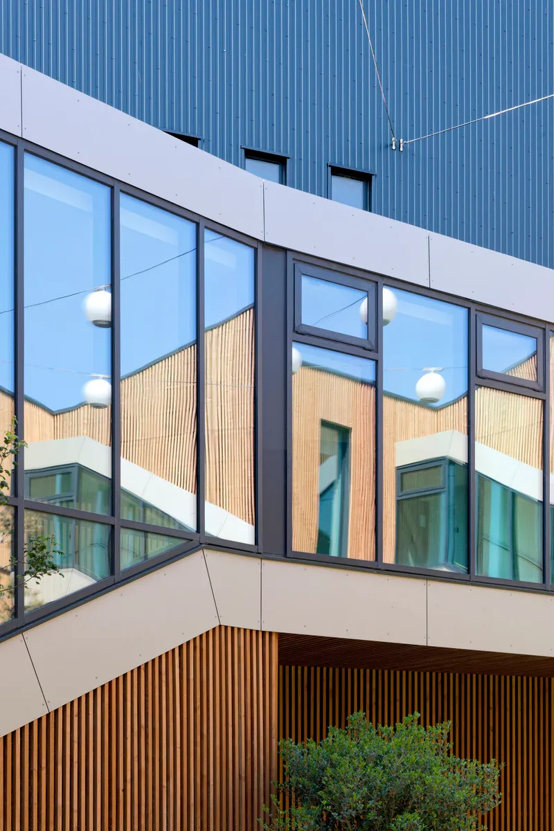 Corner detail showing reflective glass curtainwall with timber cladding visible in the mirrored surface