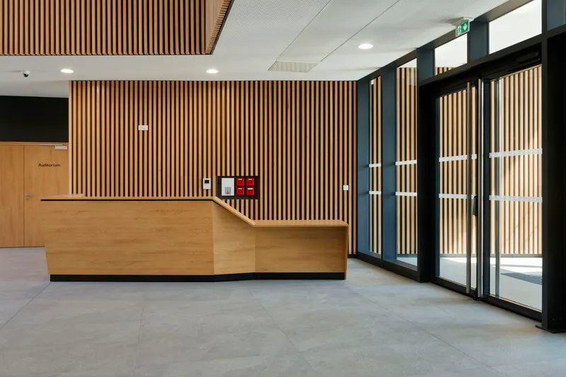 Reception desk with vertical timber slat wall and black-framed glazed entrance doors