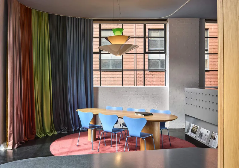 Meeting area framed by multicolored curtains with tiered pendant light hanging over timber table
