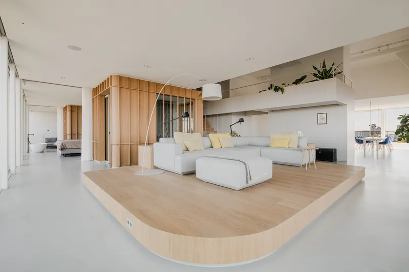 Open living area with curved timber platform hosting a sectional sofa and vertical slat screens