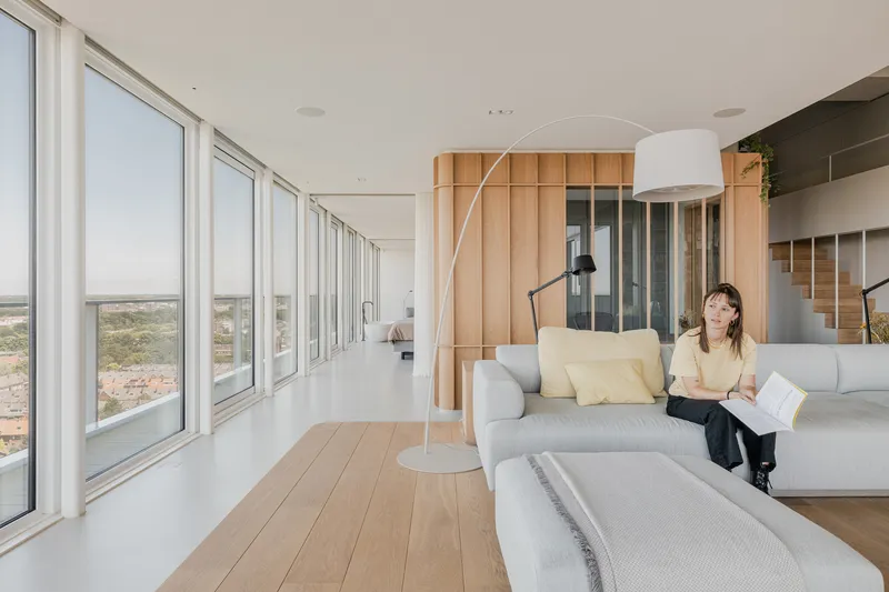 Living room with arcing floor lamp and a person reading on the sofa by panoramic windows
