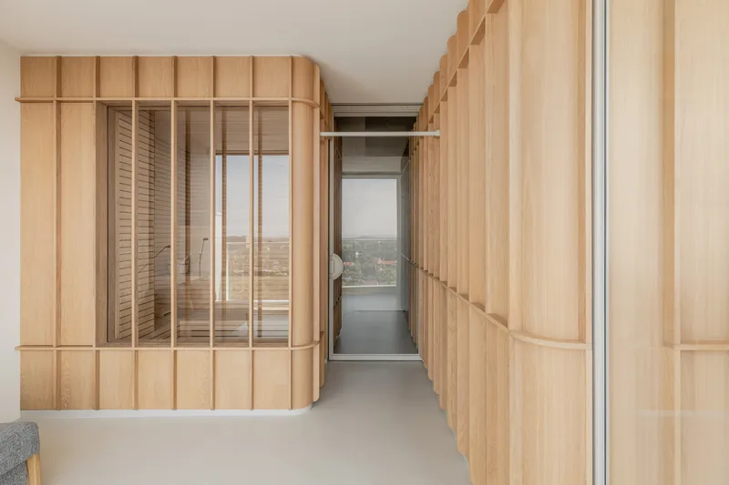 Corridor flanked by curved timber paneling with glass inserts revealing a distant cityscape