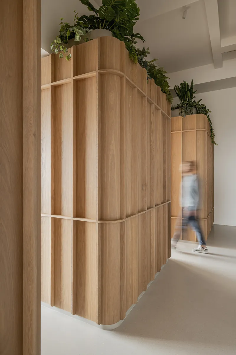 Curved timber storage unit topped with planters and a blurred figure passing by