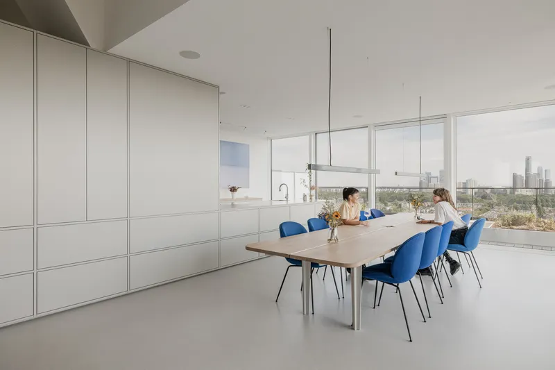 Dining area with blue chairs and two people seated at table near floor-to-ceiling windows