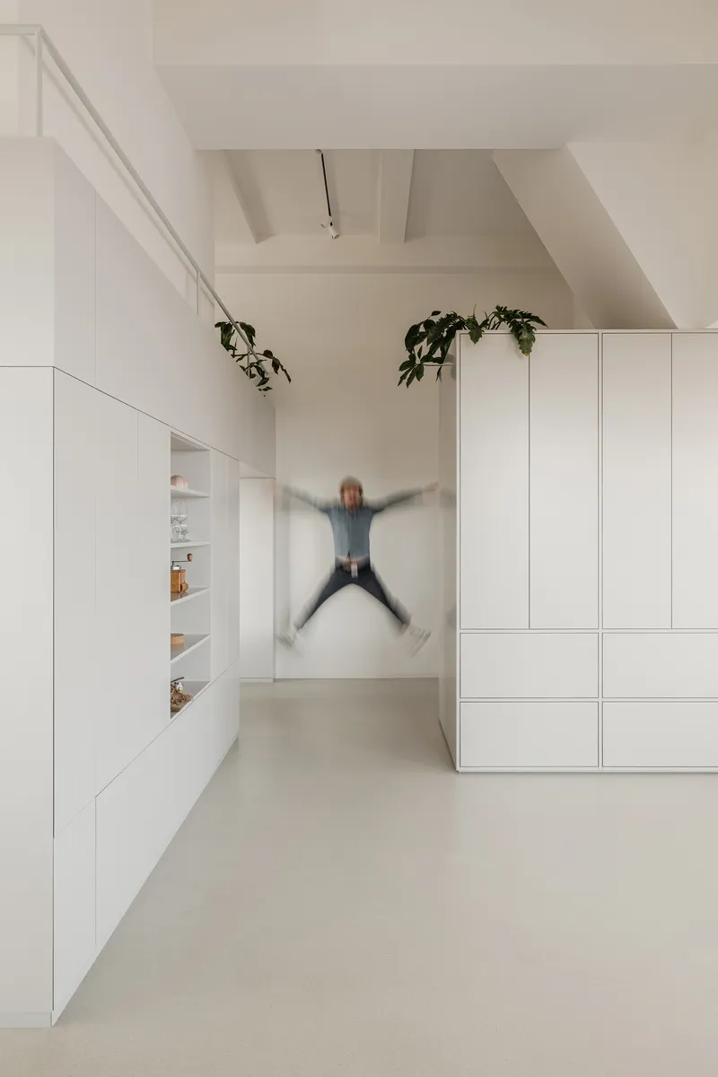 White hallway with built-in cabinetry and a person jumping mid-air beneath exposed ceiling beams