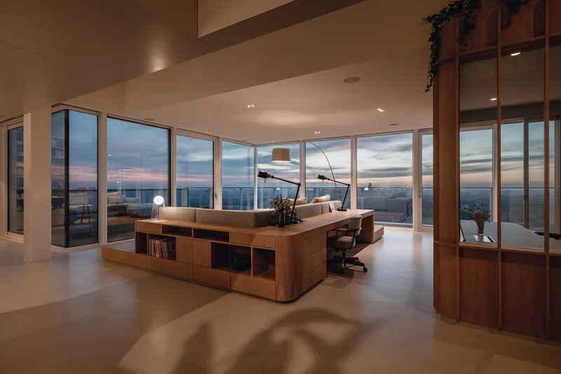 Open living space with floor-to-ceiling glazing overlooking the city at dusk