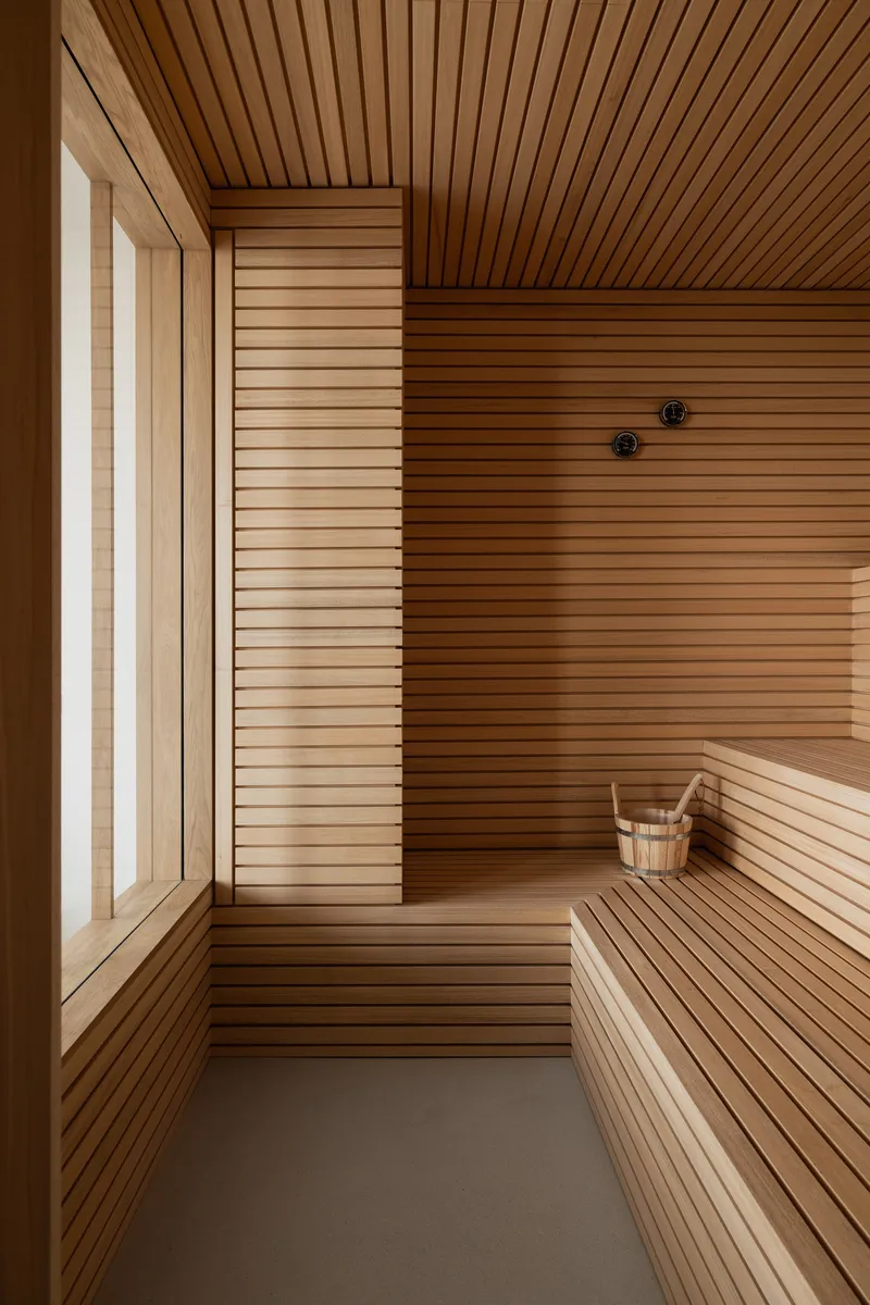 Sauna interior with horizontal timber slat walls, benches, and a wooden bucket on the floor
