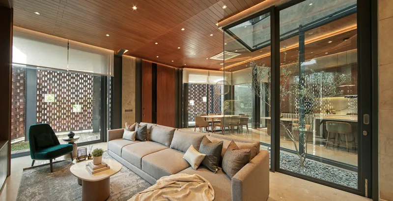 Living room with timber ceiling and glass walls overlooking a pebbled courtyard with a single tree