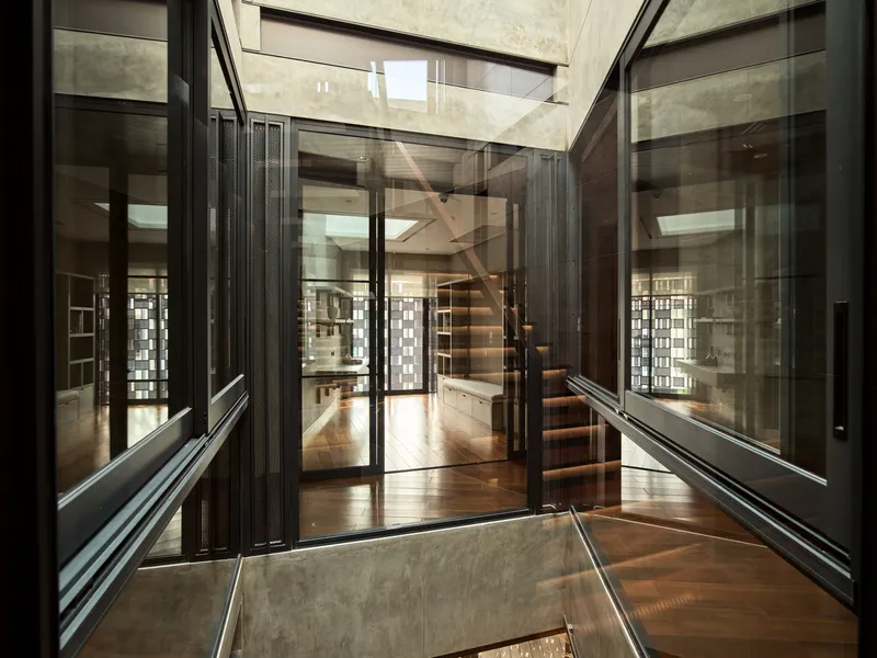 Interior view through glass partitions showing a cantilevered timber staircase beneath a skylight