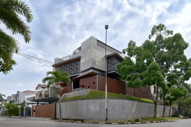 Corner view showing layered concrete walls and basketweave brick screens beside a mature tree