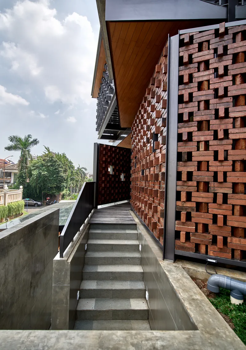 Concrete staircase running alongside a basketweave terracotta brick screen wall under cloudy skies