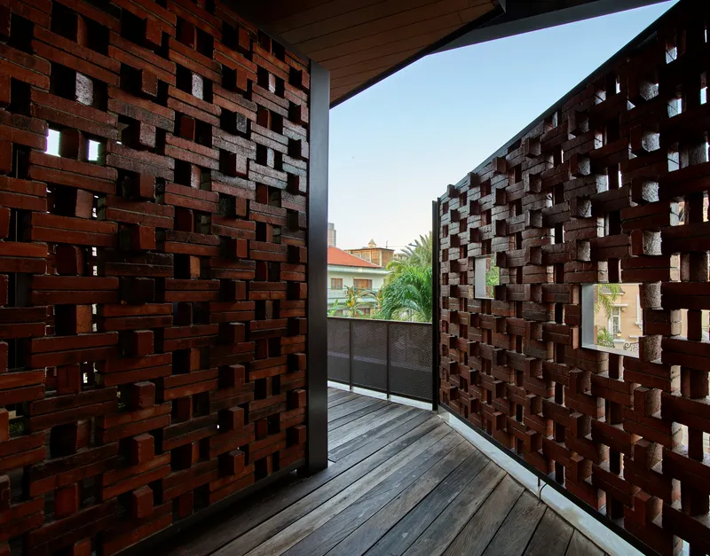 Upper balcony framed by perforated brick screens with view to palm trees and neighboring rooftops