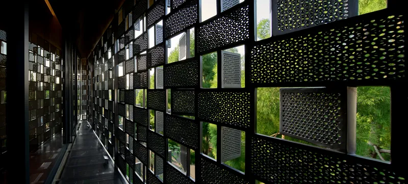 Interior corridor with perforated metal screen wall casting dappled shadows and framing green foliage outside