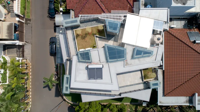Aerial view of white rooftop with geometric skylights and small planted courtyards among neighboring tile roofs
