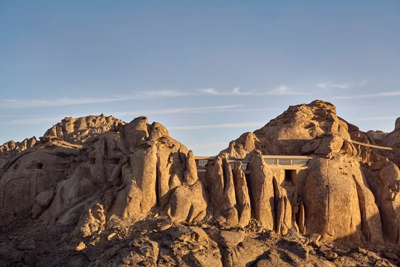 Concrete roof structure rising between jagged rock outcroppings in golden afternoon light