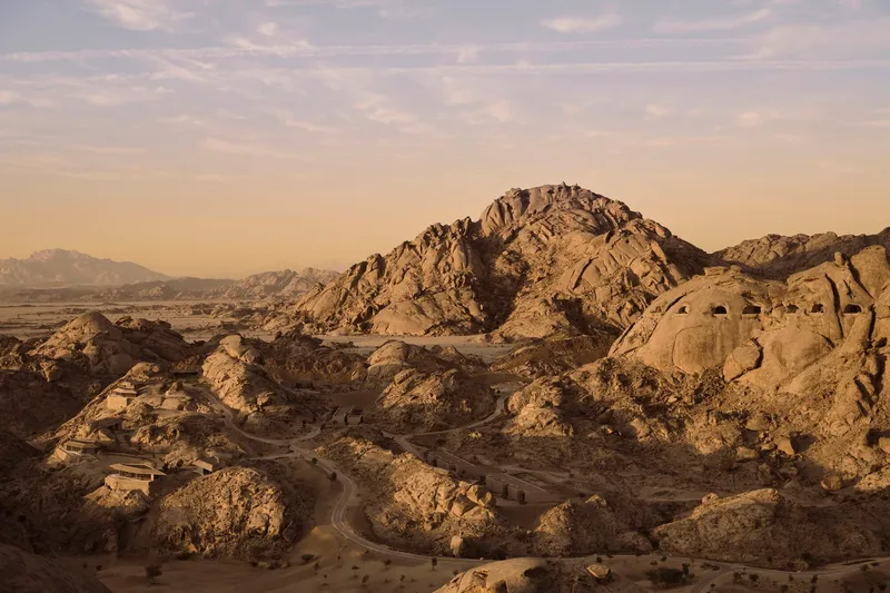 Aerial view of a desert valley with low-rise structures nestled among eroded rock formations at golden hour