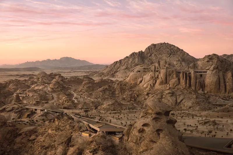 Elevated concrete bridge extending across the desert terrain toward a carved stone outcrop at dusk