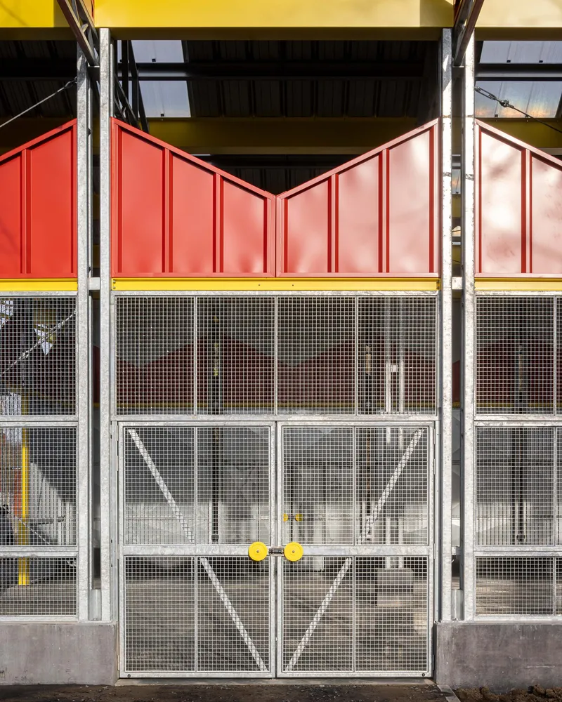 Mesh screen doors with diagonal bracing beneath red corrugated panels in afternoon sunlight