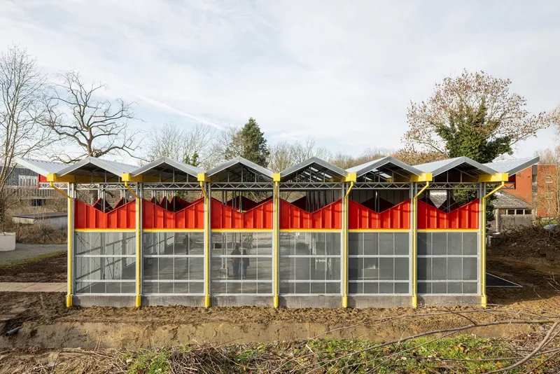 Front elevation showing six bays with red corrugated panels and glazed lower sections under a cloudy sky