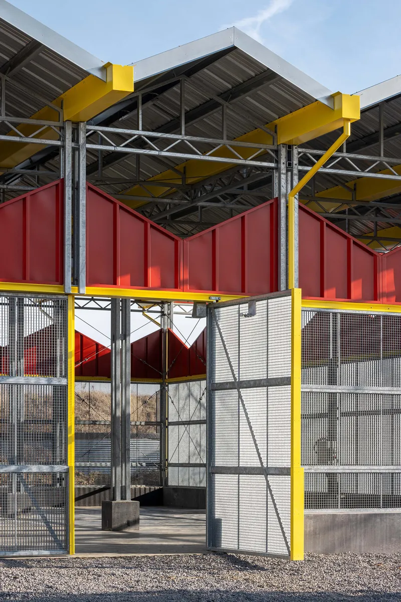Detail of the structural frame showing yellow steel beams supporting red panels and metal mesh screening