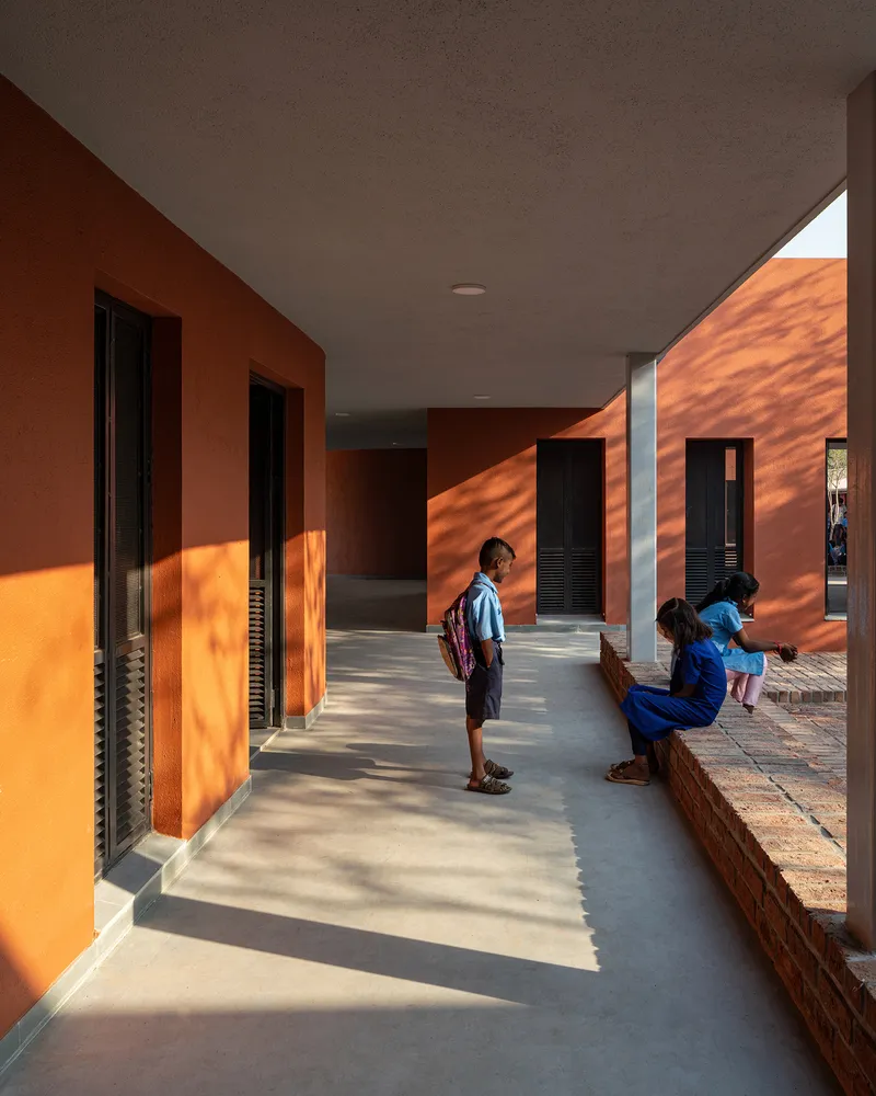 Covered corridor with terracotta walls and deep shadows cast by afternoon sunlight across polished concrete floor