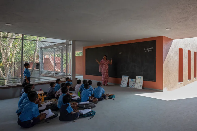 Semi-open learning space with chalkboard wall and mesh-screened opening framing courtyard beyond
