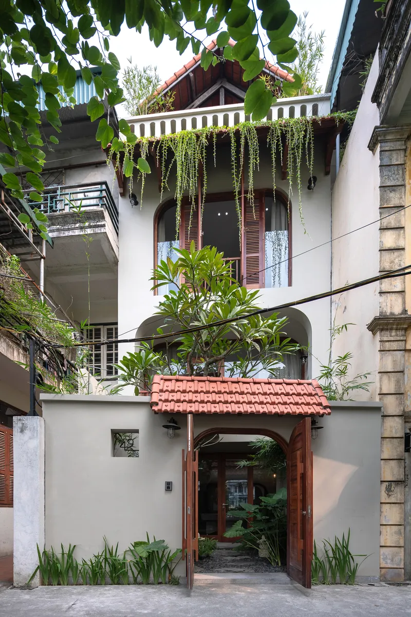 Street facade with timber-framed entry gate, terracotta tile roof and cascading plants from upper balcony