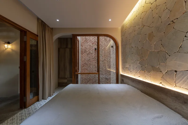 Arched timber doorway with herringbone brick infill facing a backlit stone feature wall