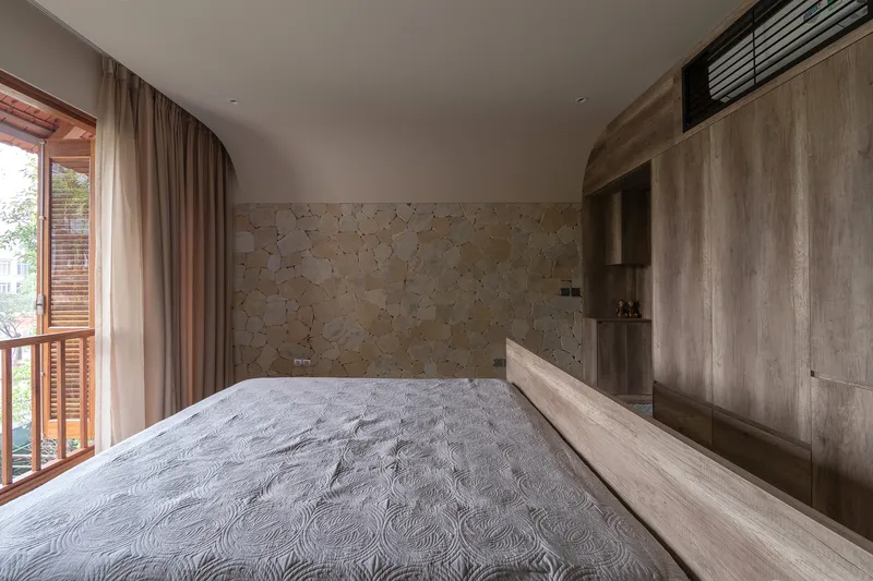 Bedroom with stone accent wall and timber joinery visible through louvered balcony doors