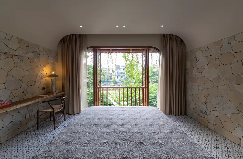Bedroom with arched curtain recess, timber balcony doors and patterned stone walls
