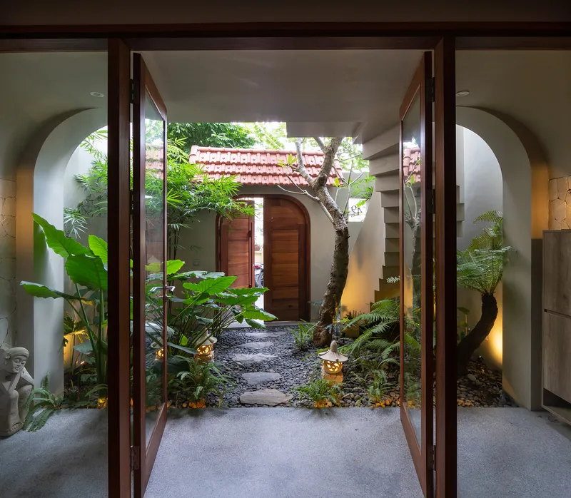 View through open timber doors into courtyard garden with arched white walls framing the passage
